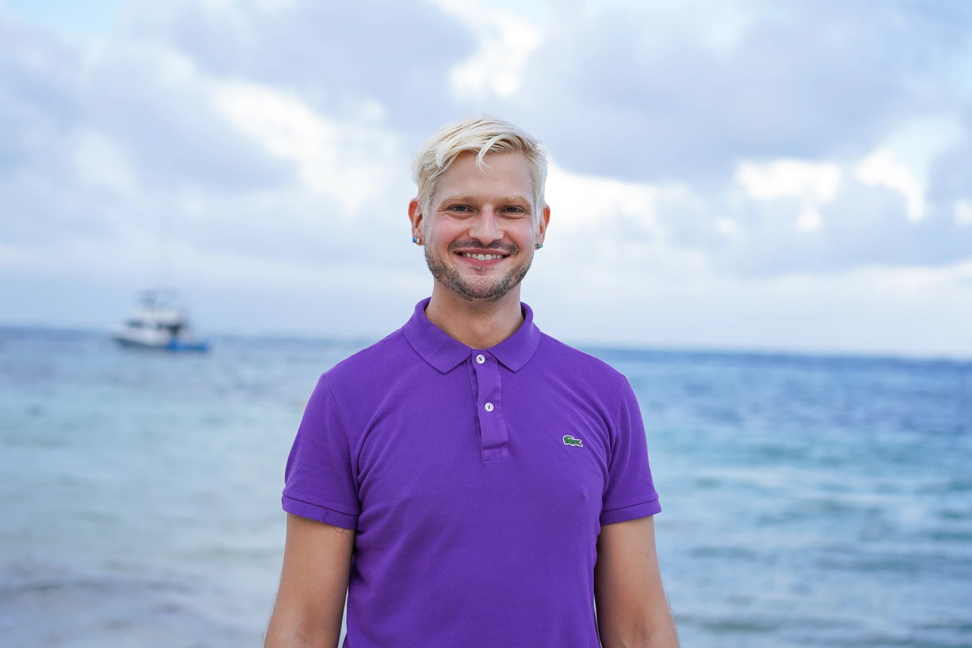 Dr. Derek Austin smiling by the ocean in a purple polo